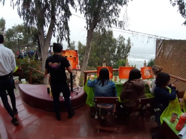 foto de una sesión de pintura de Paint in Bar realizada en Barranco/Lima, Perú, con el artista parado y los clientes sentados, de espalda para la foto y viendo el mar a su frente.
